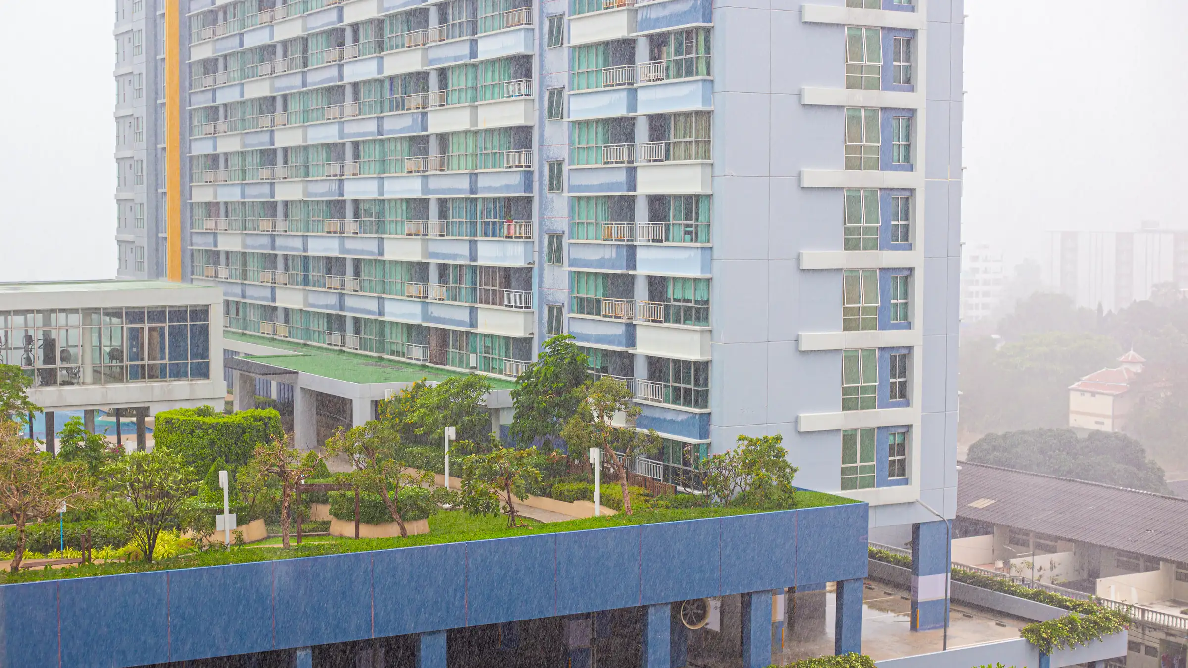 Immeuble de copropriété surplombant une terrasse avec piscine paysagée, par un jour de pluie en Thaïlande