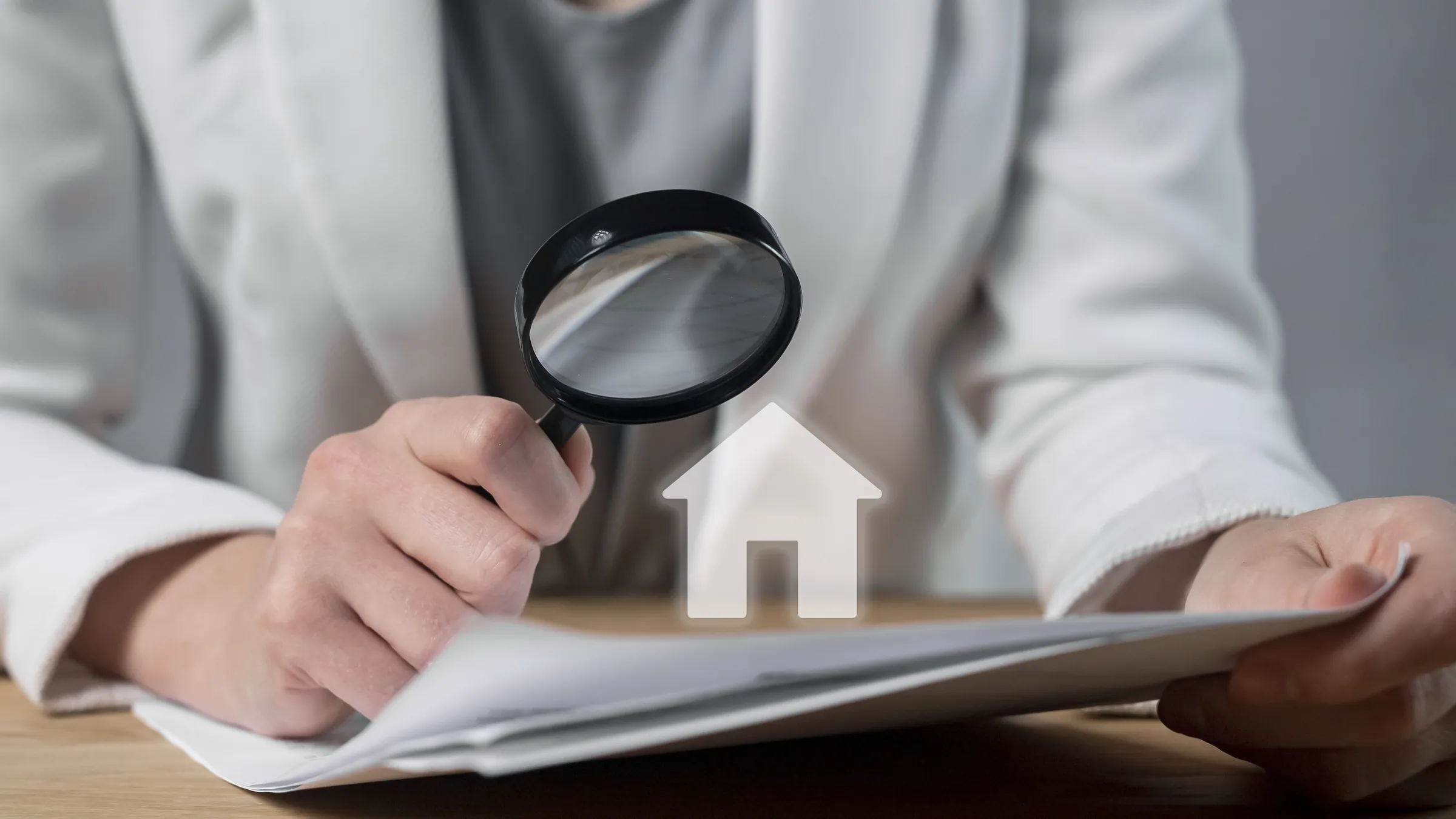 Mains tenant une loupe au-dessus d’un contrat d’achat immobilier, à côté d’une petite maquette de maison