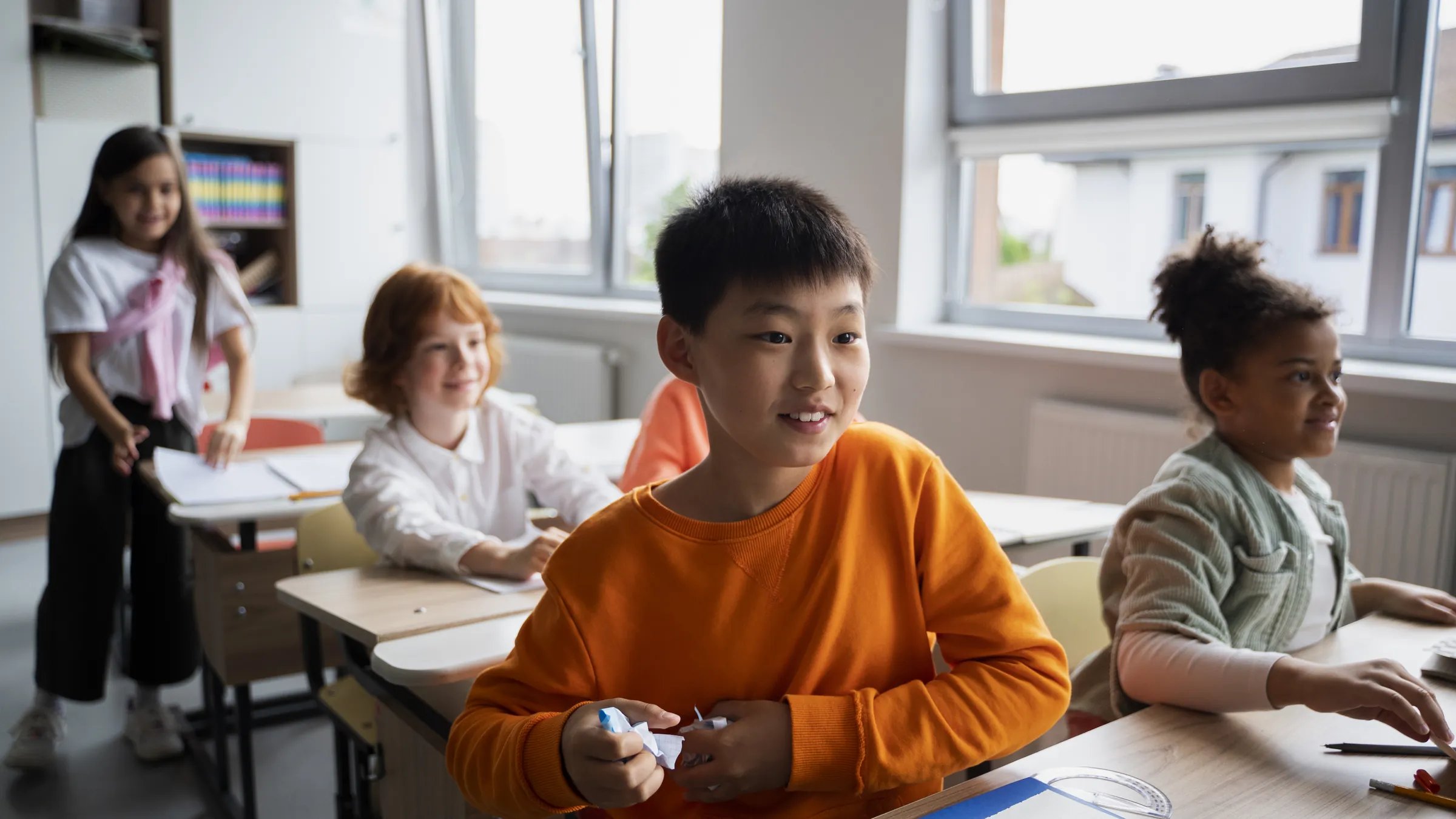 Enfants d’origines diverses travaillant à leur pupitre dans une salle de classe lumineuse