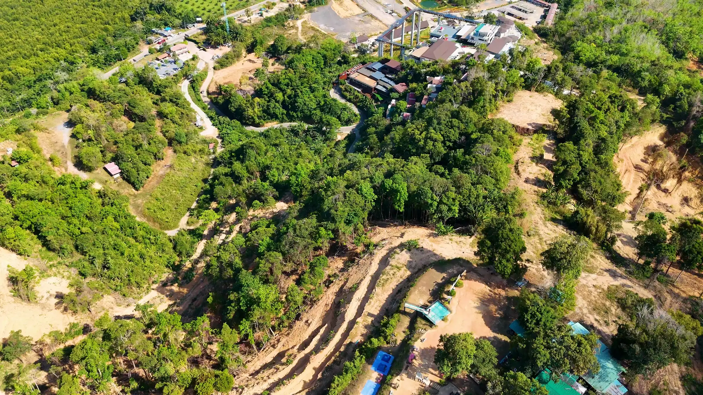 Vue aérienne d’une colline verdoyante entaillée de nouvelles routes d’accès et de parcelles défrichées, plantations à l’arrière-plan