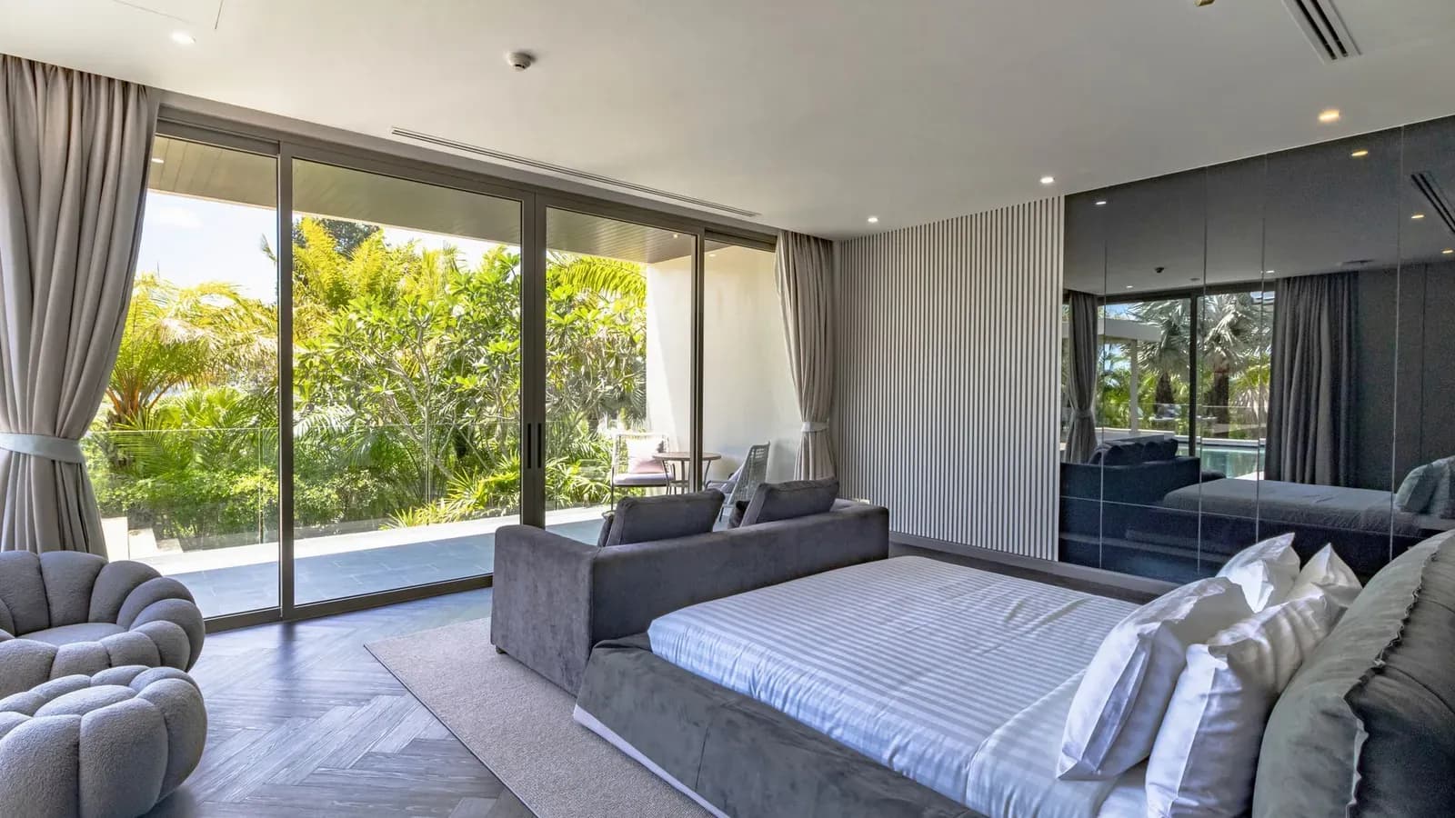 Une chambre de villa aux baies vitrées toute hauteur ouvertes sur un jardin tropical
